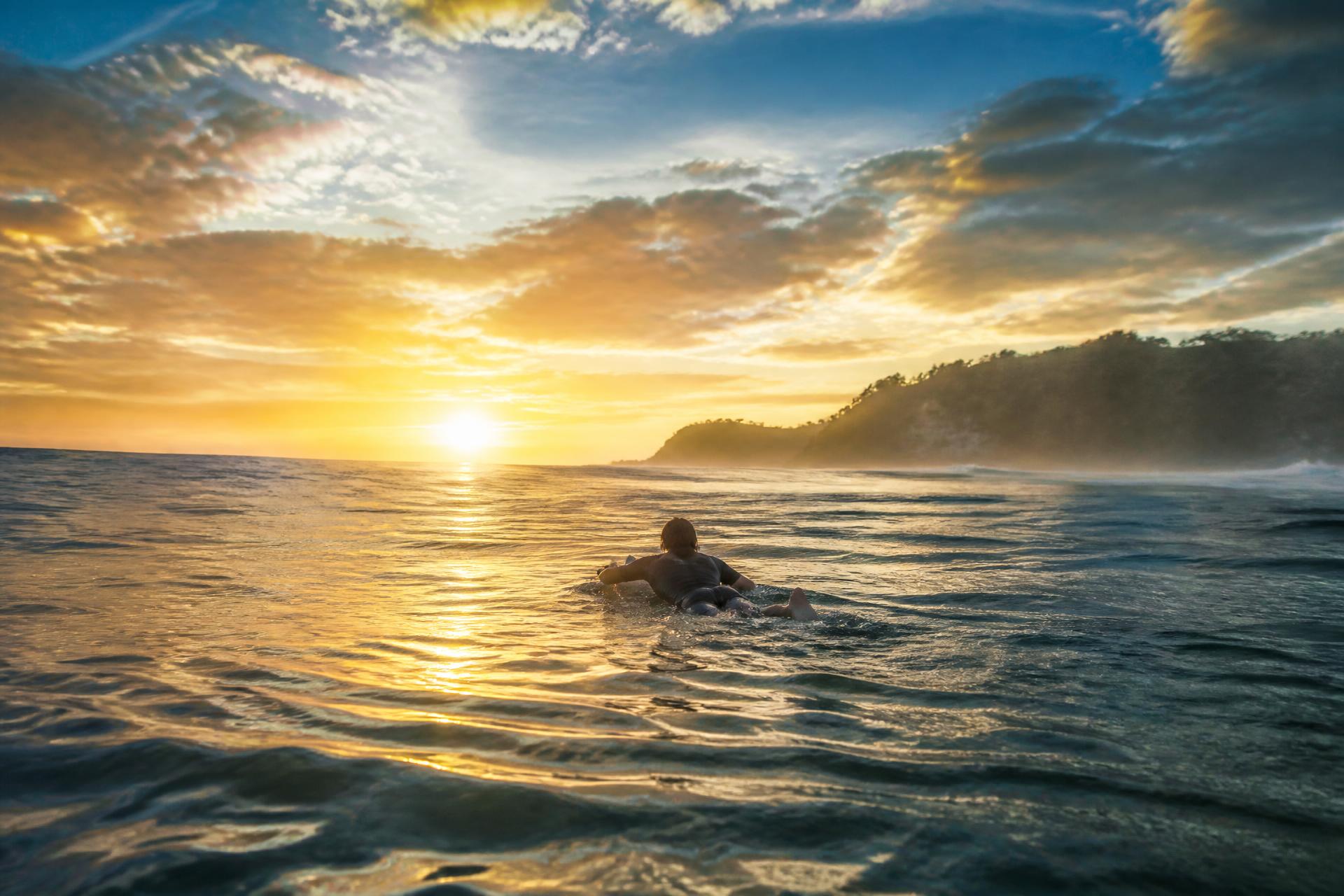 Surfer paddling toward a glowing sunrise horizon